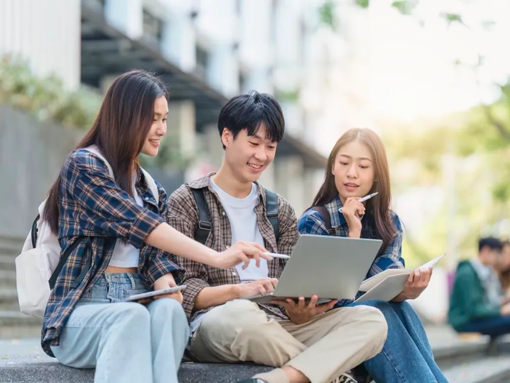 นักศึกษาต่างชาติทำงานกลุ่มกับโน้ตบุ๊กและสมุดบนบันไดในมหาวิทยาลัยจีน
