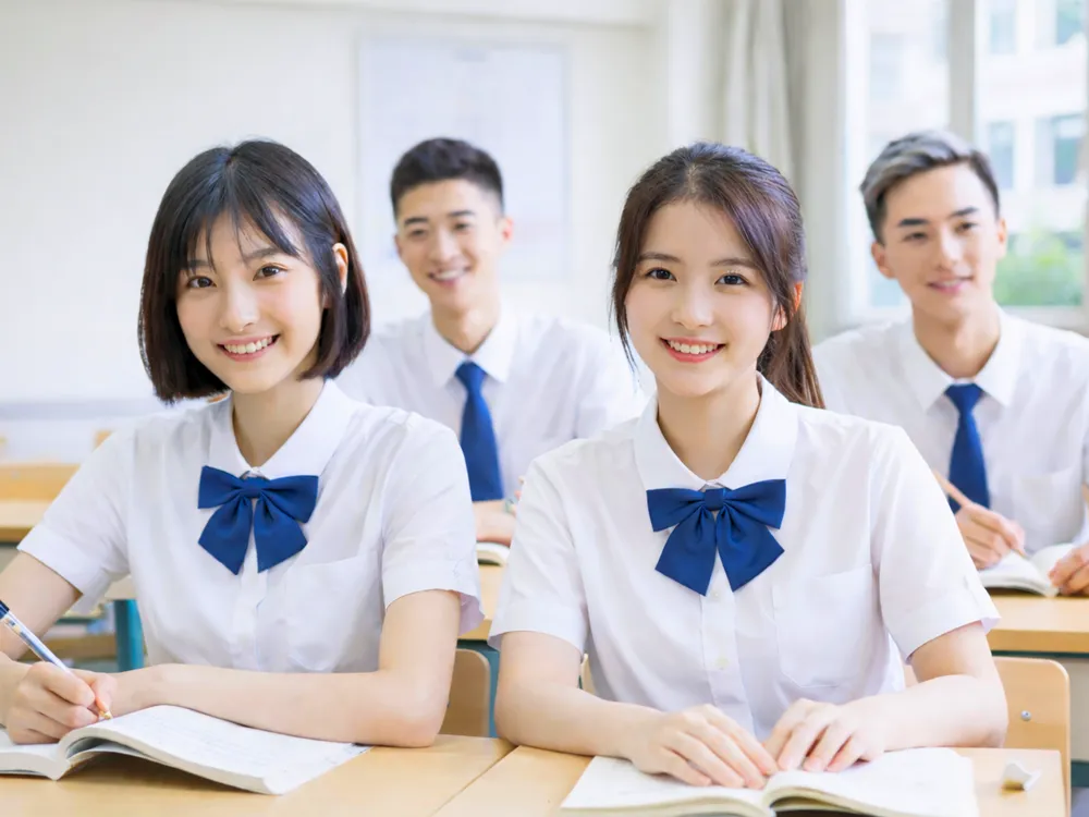นักเรียนมัธยมปลายนั่งเรียนในห้องเรียนจีน สวมชุดยูนิฟอร์มสีขาวและเนคไทน้ำเงิน