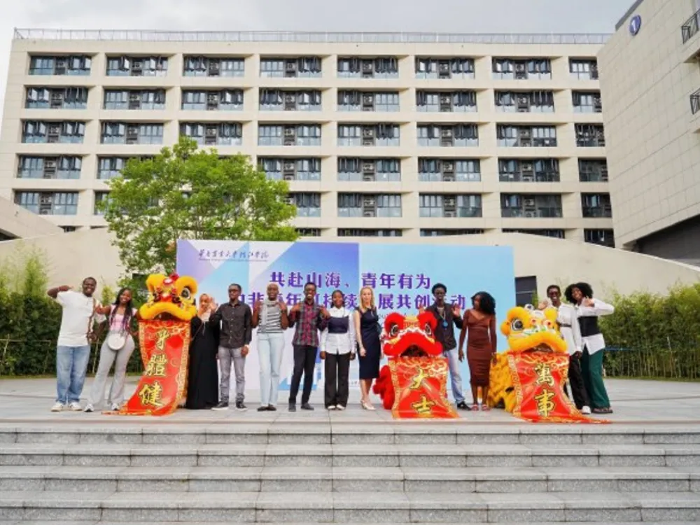 กลุ่มนักศึกษาและผู้ร่วมงานยืนถ่ายภาพหน้าตึกหลักของ South China Agricultural University พร้อมการแสดงเชิดสิงโตสีเหลืองและสีแดงในงานเฉลิมฉลองมหาวิทยาลัย