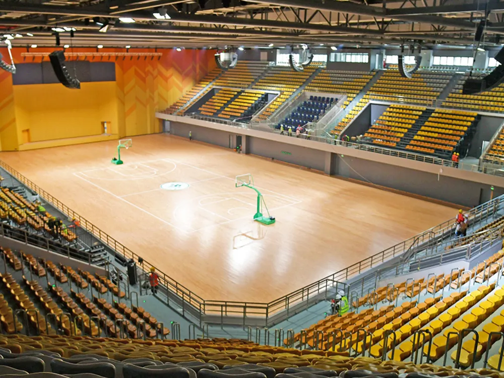 สนามบาสเกตบอลในร่มของ South China Agricultural University พื้นไม้พร้อมแป้นบาสสีเขียวและที่นั่งสีเหลือง–น้ำเงินหลายชั้น