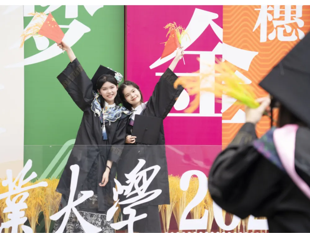 นักศึกษาสวมชุดครุยและหมวกรับปริญญาเฉลิมฉลองหน้าฉากสีสันสดใสในงานรับปริญญาของ South China Agricultural University