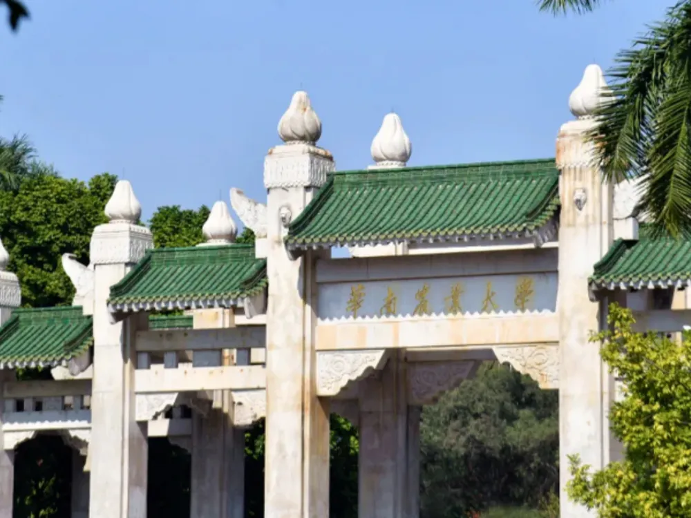 ซุ้มประตูสถาปัตยกรรมจีนดั้งเดิมของ South China Agricultural University หลังคากระเบื้องสีเขียว ประดับลวดลายทอง รายล้อมด้วยต้นไม้และท้องฟ้าแจ่มใส