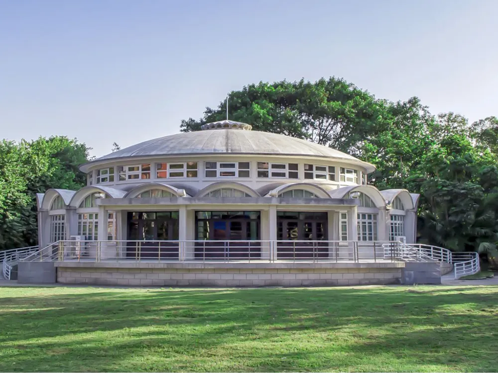 อาคารทรงกลมสมัยใหม่ของ South China Agricultural University หลังคาโดม หน้าต่างโค้ง รายล้อมด้วยต้นไม้และสนามหญ้าเขียวชอุ่ม