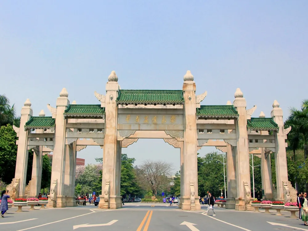 ซุ้มประตูหินสถาปัตยกรรมจีนดั้งเดิมของ South China University of Technology หลังคากระเบื้องสีเขียว ประดับลวดลายทอง มีผู้คนเดินผ่านด้านหน้า