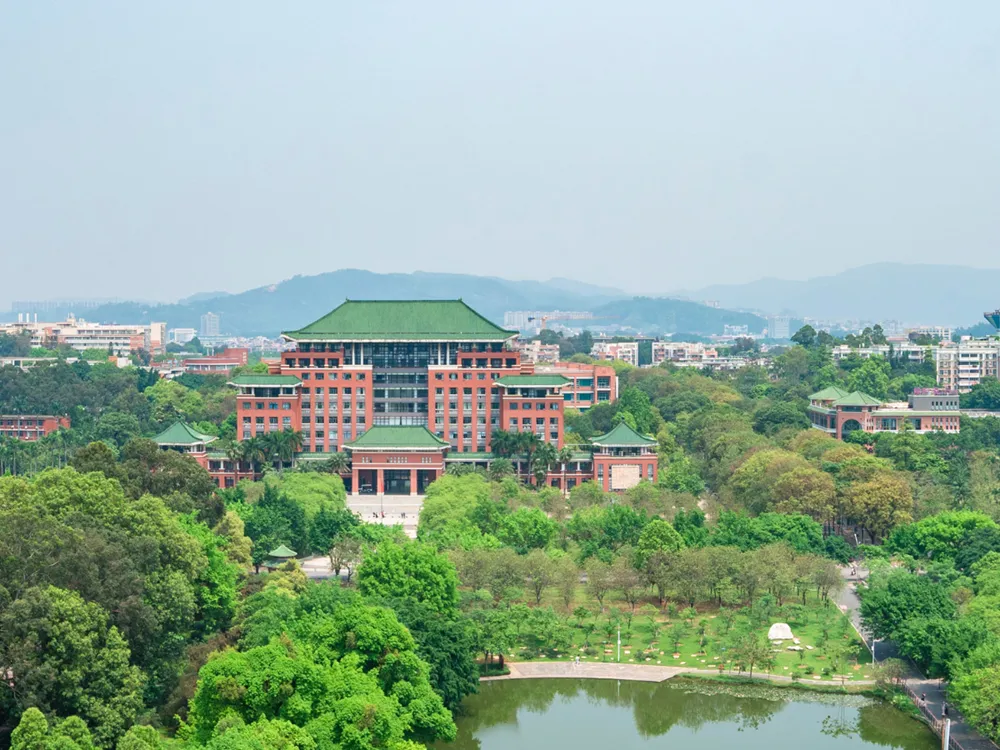 ภาพมุมสูงของวิทยาเขต South China Agricultural University อาคารอิฐสีแดงหลังคาสีเขียว รายล้อมด้วยสวน ต้นไม้ และบ่อน้ำกลางมหาวิทยาลัย