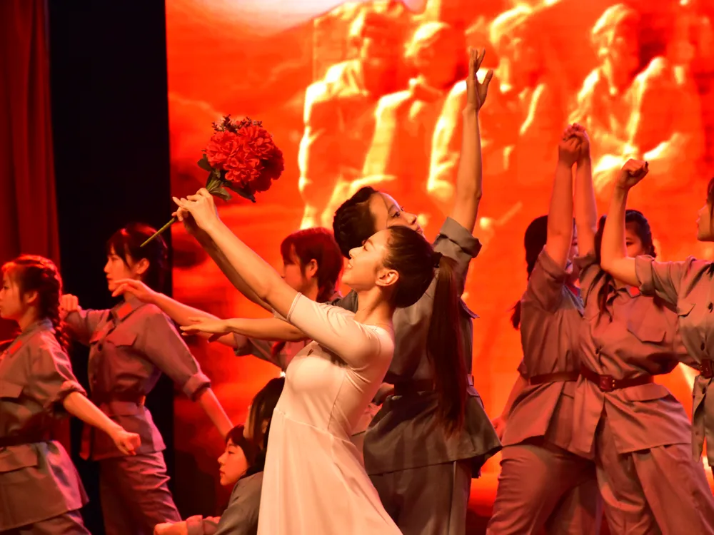 การแสดงศิลปะบนเวที Shenyang City University นักแสดงถือดอกไม้แดงท่ามกลางแสงสีแดงเข้ม