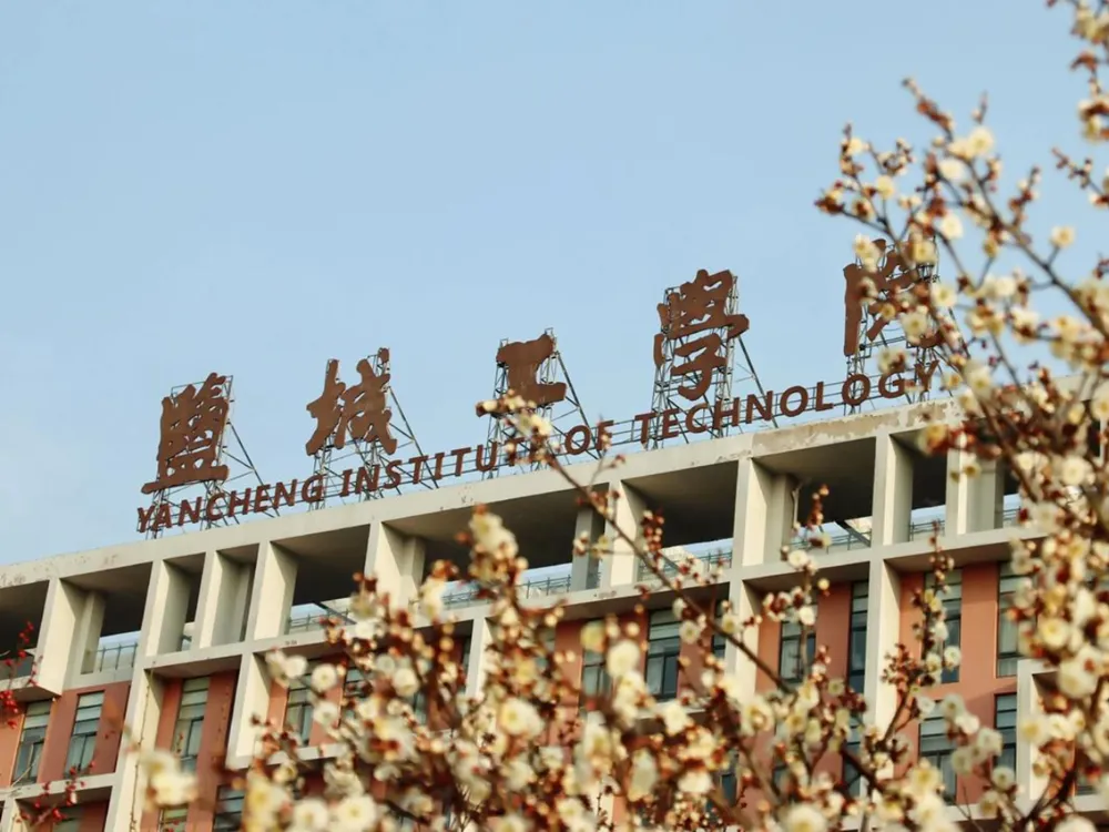 อาคารมหาวิทยาลัย Yancheng Institute of Technology พร้อมป้ายชื่อภาษาจีนและอังกฤษ ท่ามกลางดอกไม้บานฤดูใบไม้ผลิ