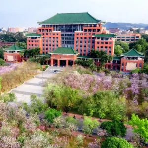 อาคารหลักของ South China Agricultural University เมืองกว่างโจว สถาปัตยกรรมจีนดั้งเดิมหลังคากระเบื้องสีเขียว รายล้อมด้วยต้นไม้และดอกไม้บานในฤดูใบไม้ผลิ
